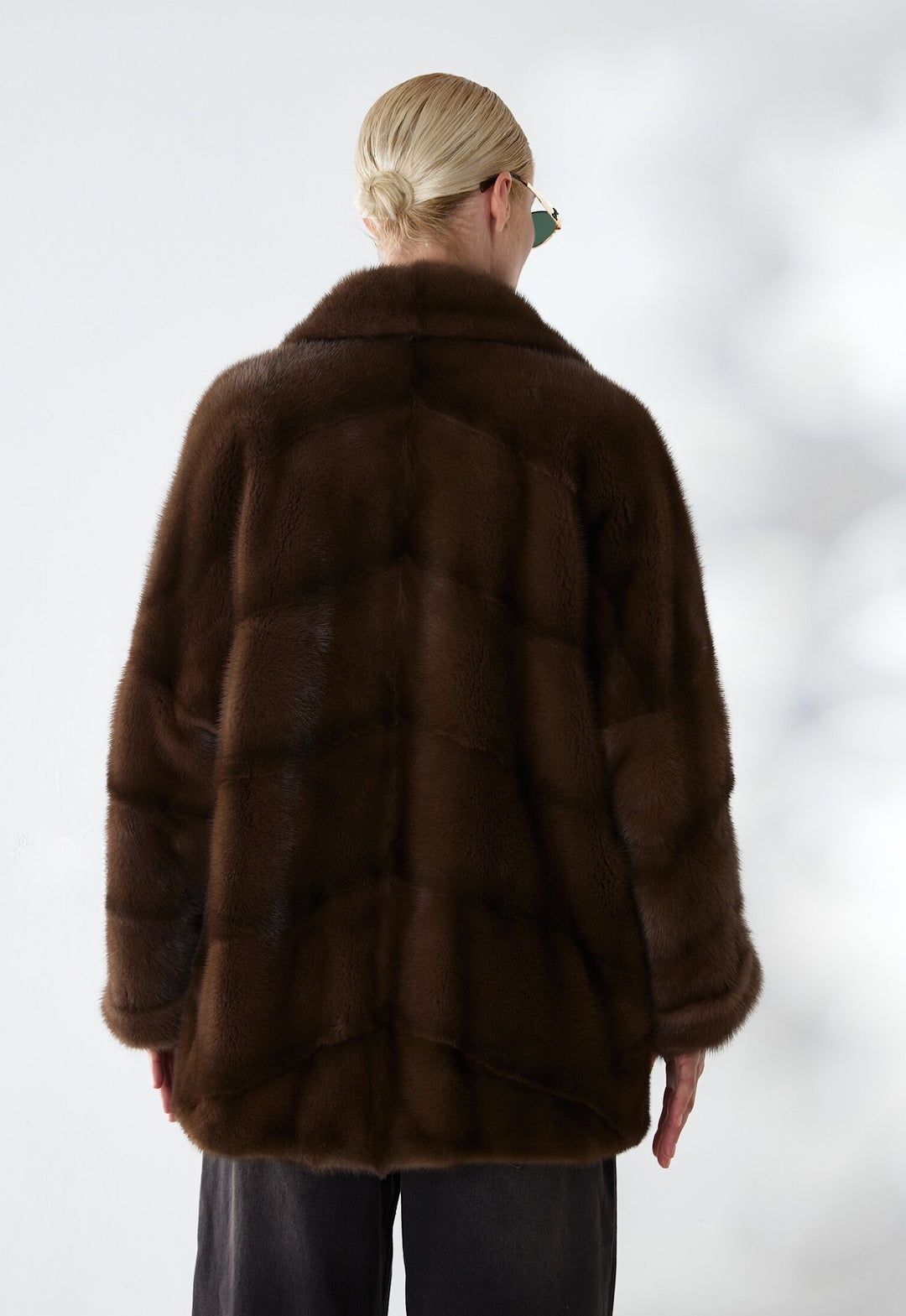 A woman elegantly wears a short dark brown mink fur coat, highlighting its rich texture and luxurious sheen for a chic, timeless look.