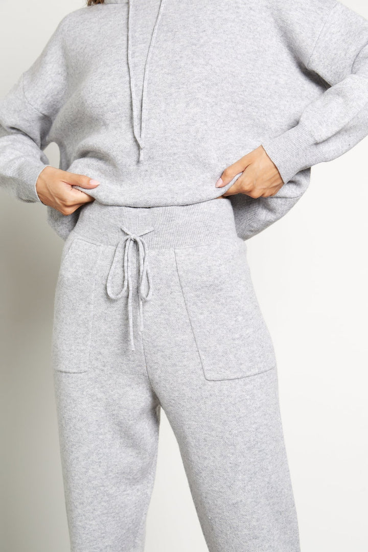 A woman wearing a grey wool cashmere tranksuit consisted of a sweater with fox fur trim and matching cashmere wool trousers.