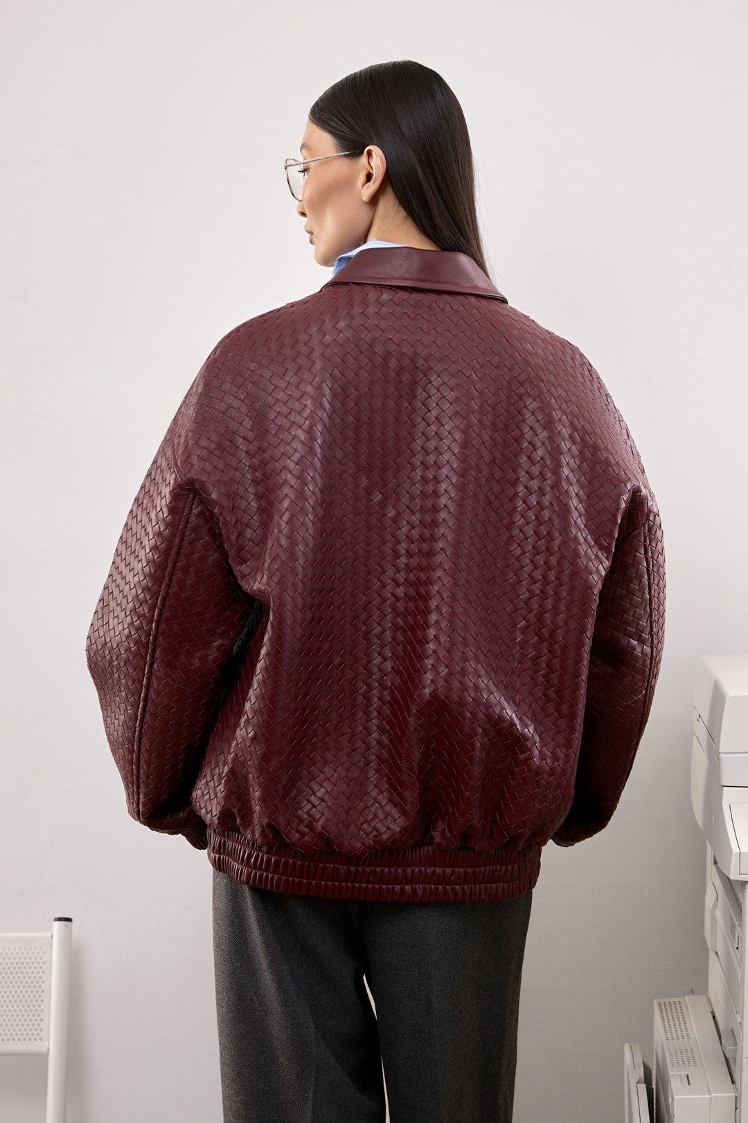 A woman in a burgundy bomber jacket featuring clean lines and side pockets, blending casual ease with contemporary sophistication.