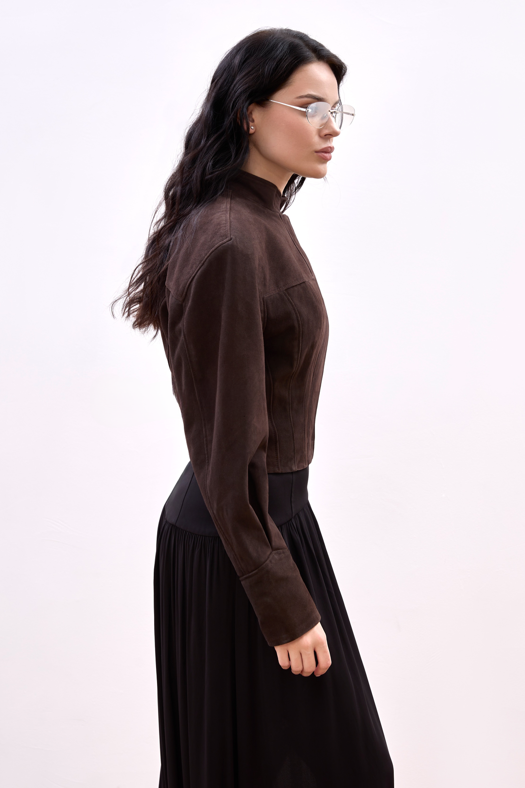 A woman in a striking espresso-hued suede jacket, styled with minimalist precision, including a clean front, cropped cut, and a fit that defines the waist and shoulders.