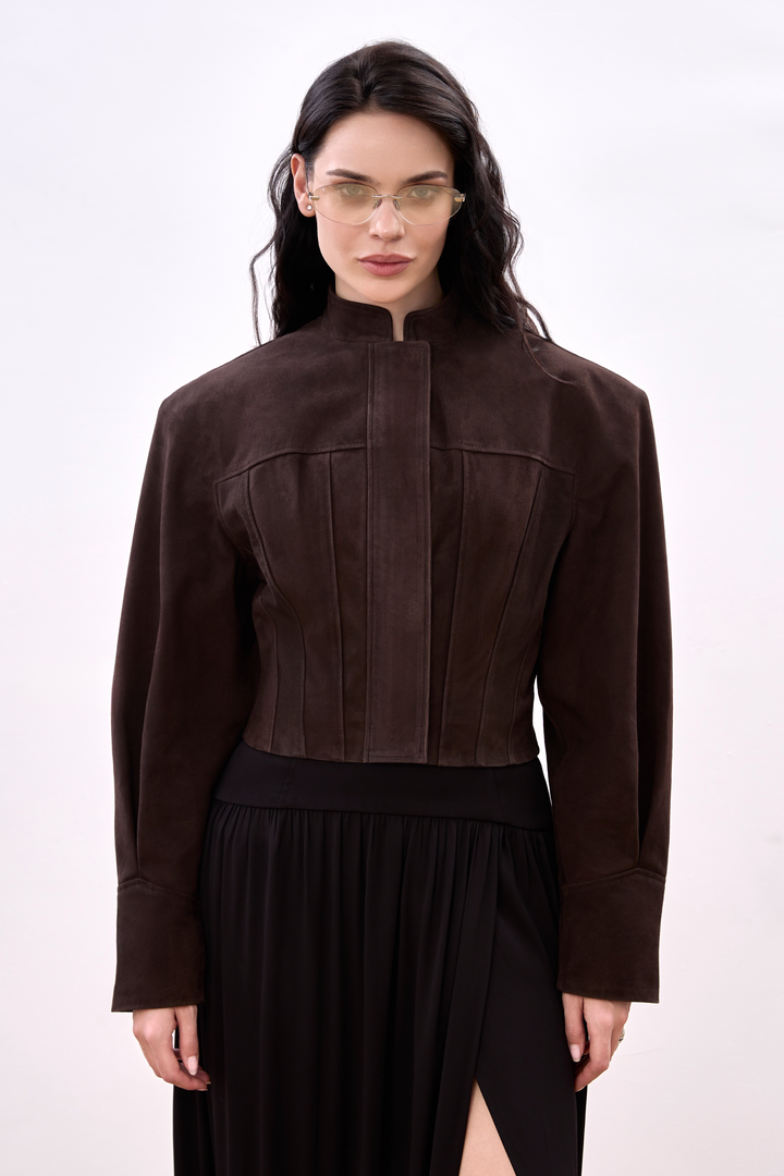 A woman wearing a sharp, espresso-colored suede jacket with a cropped silhouette, tailored to accentuate the waist and shoulders with clean, minimalist lines.