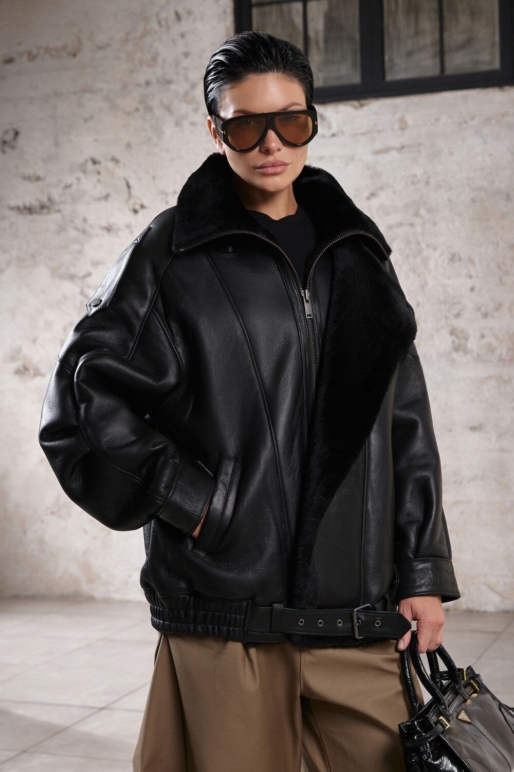 A woman wearing an oversized sheepskin jacket with a high neck and relaxed fit, featuring a plush shearling lining that adds luxury to its sporty yet chic design.