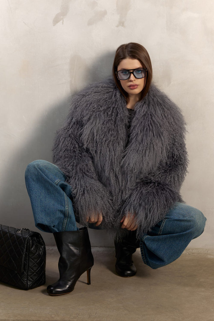 A woman models a stunning grey Mongolian coat made from 100% genuine Mongolian fur, featuring a dramatic collar, snap front closures, side slit pockets, and a satin and leather inner lining.