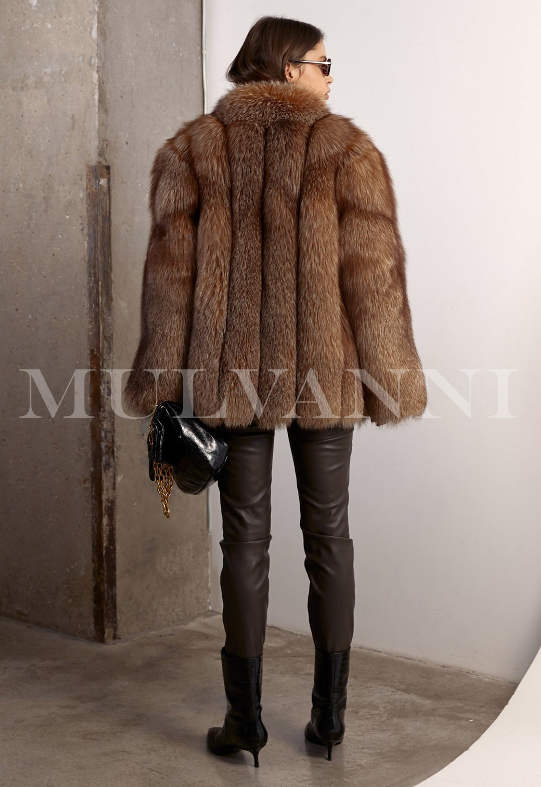 The voluminous silhouette of the genuine fox fur coat is complemented by brown leggings and a black leather bag, creating a sophisticated and cozy winter outfit.