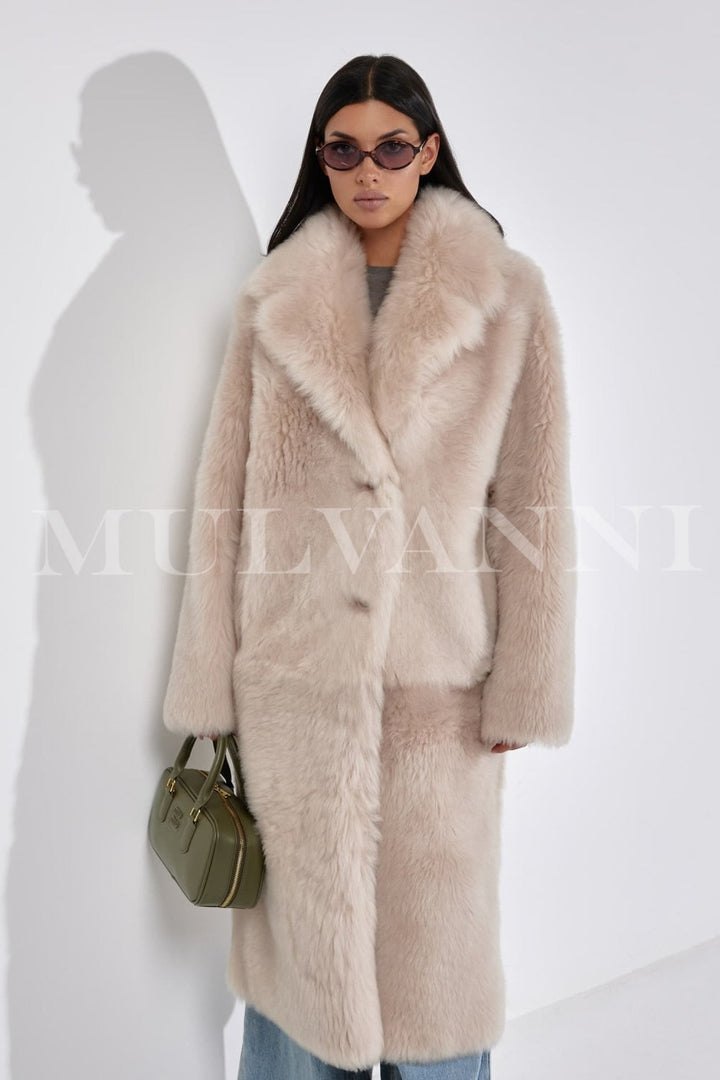 The woman models a maxi shearling coat featuring a structured fit, plush interior, and refined detailing for a chic winter look.