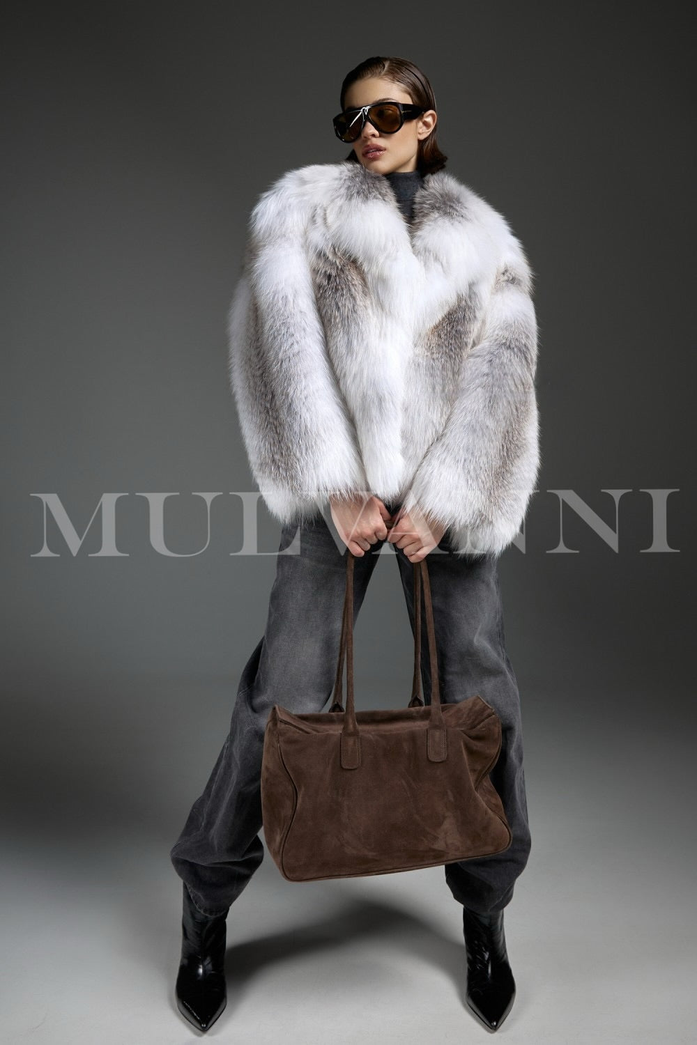 Woman elegantly wears a luxurious Arctic Crossed Fox Fur coat paired with a brown suede handbag, combining rich textures for a refined winter look.