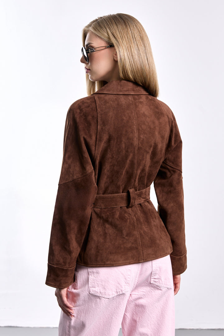 A woman seen from the back wearing a brown suede jacket with a belted waist, showcasing its tailored, cropped silhouette and elegant structure that blends modern style with timeless sophistication.