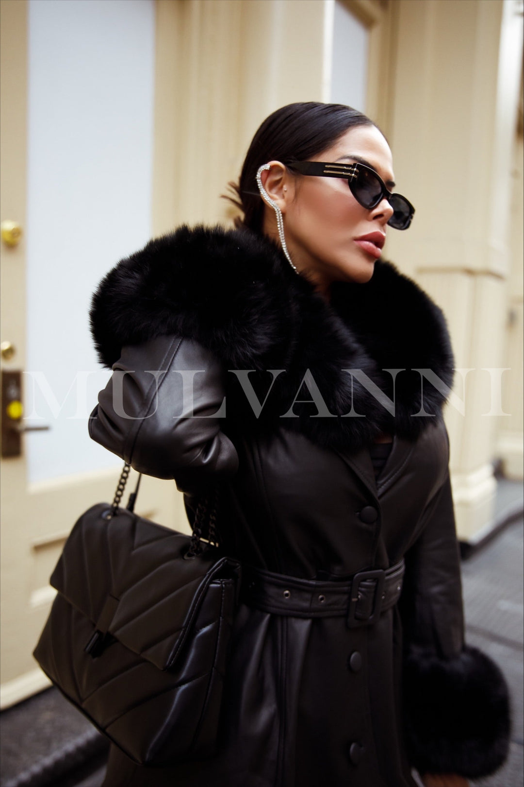 This black leather trench coat with a dramatic black fox fur collar and matching cuffs creates an effortlessly elegant winter look, worn by a woman embracing modern sophistication.