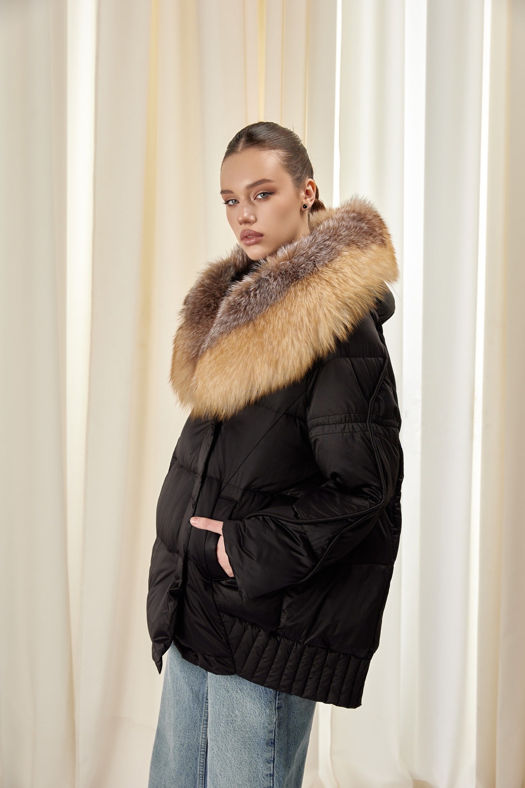 A woman wearing a black down jacket with a fluffy fox fur hood, offering a refined and cozy look for cold-weather days.