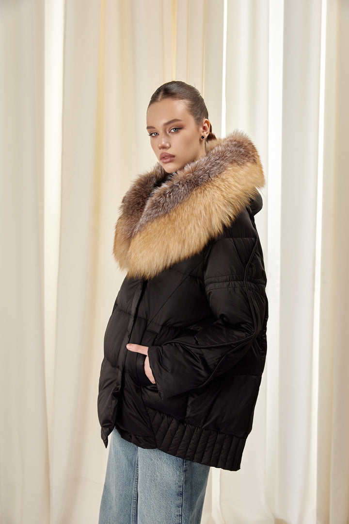 A woman wearing a black down jacket with a fluffy fox fur hood, offering a refined and cozy look for cold-weather days.