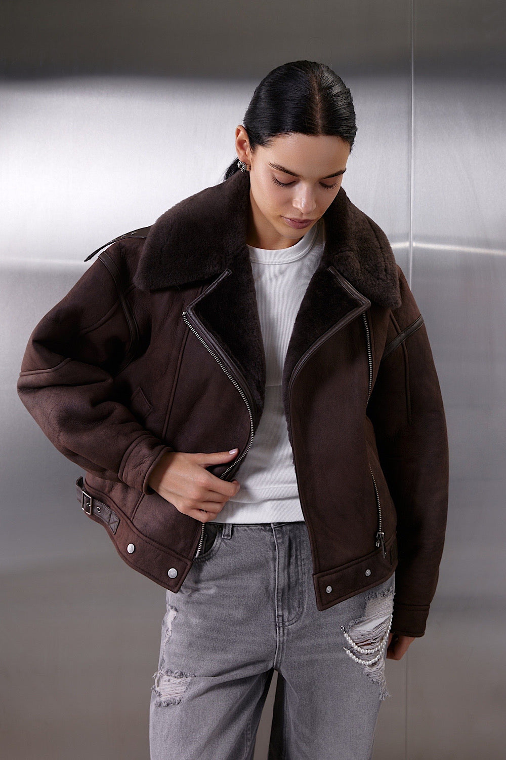 A woman wearing a classic brown aviator leather bomber jacket crafted from heavyweight sheepskin, featuring cozy shearling lining and a cropped, feminine twist on a sporty oversized style.