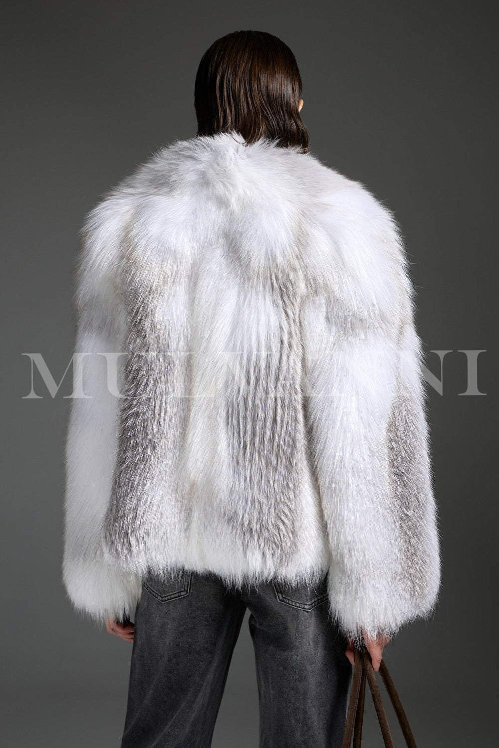 Wearing an Arctic Crossed Fox Fur coat, the woman completes her look with a chic brown suede handbag, enhancing the coat’s luxurious presence with casual refinement.