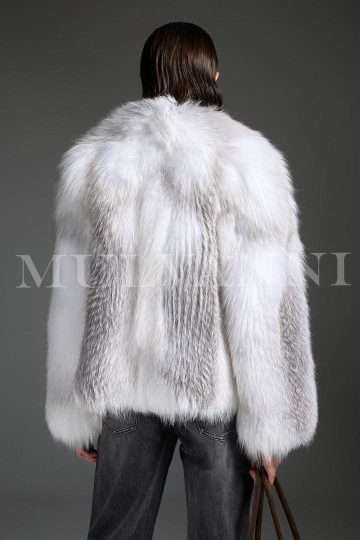 Wearing an Arctic Crossed Fox Fur coat, the woman completes her look with a chic brown suede handbag, enhancing the coat’s luxurious presence with casual refinement.