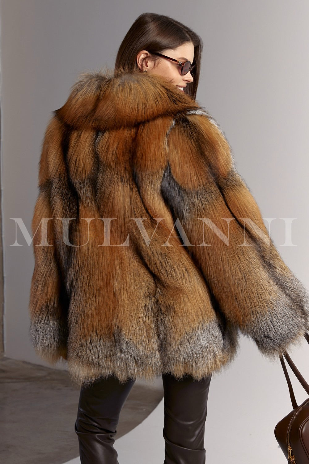 The fiery tones of the red fox fur coat contrast beautifully with the woman's brown leggings and leather handbag, resulting in a chic and cozy cold-weather outfit.