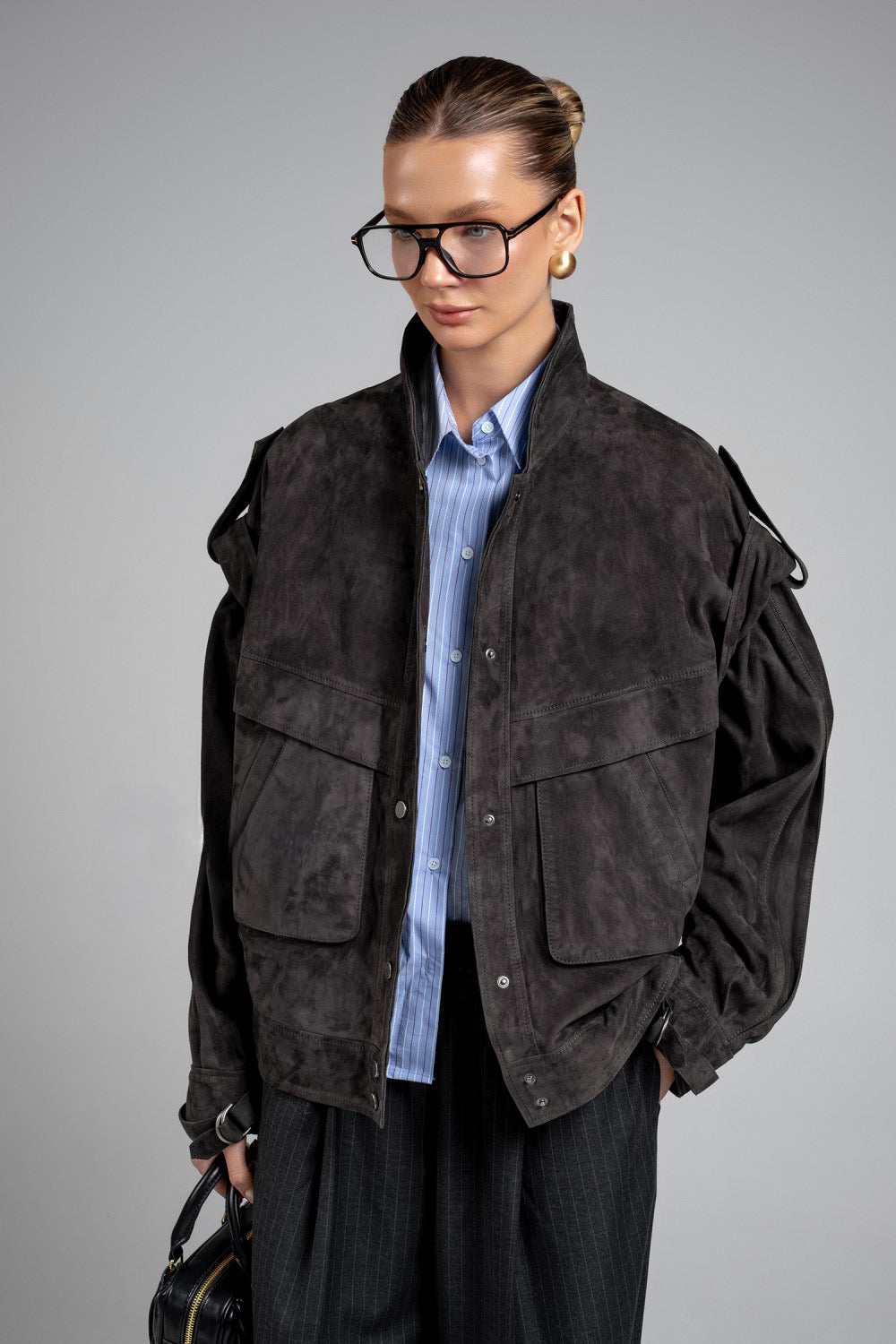 A woman wears a charcoal suede jacket crafted from soft, high-quality suede leather, featuring a flattering fit and rich hue for versatile style.