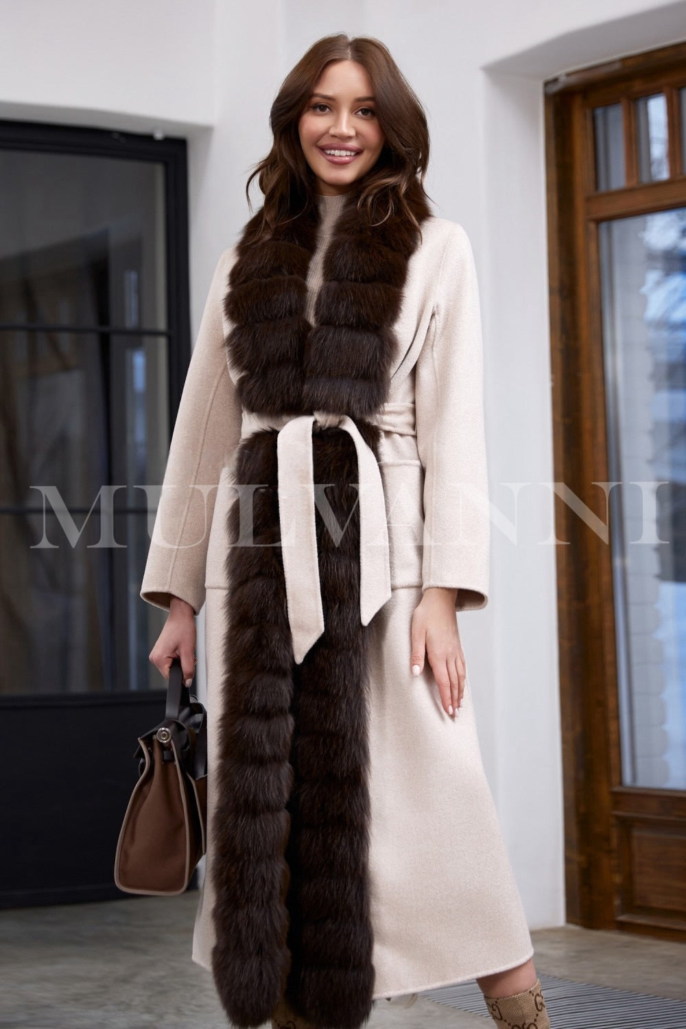 A woman wears a beige double-faced cashmere coat expertly tailored for a flawless silhouette, featuring a matching belt that cinches the waist and brown fox fur trim for elegant warmth.