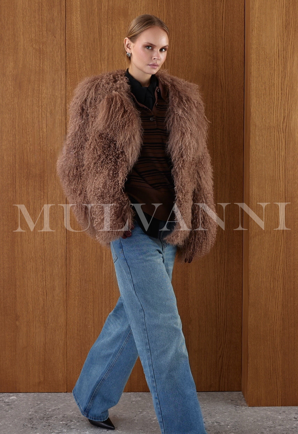 Styled in rich brown, the woman showcases a full Mongolian fur coat with a plush texture, front snap closures, and relaxed sophistication.