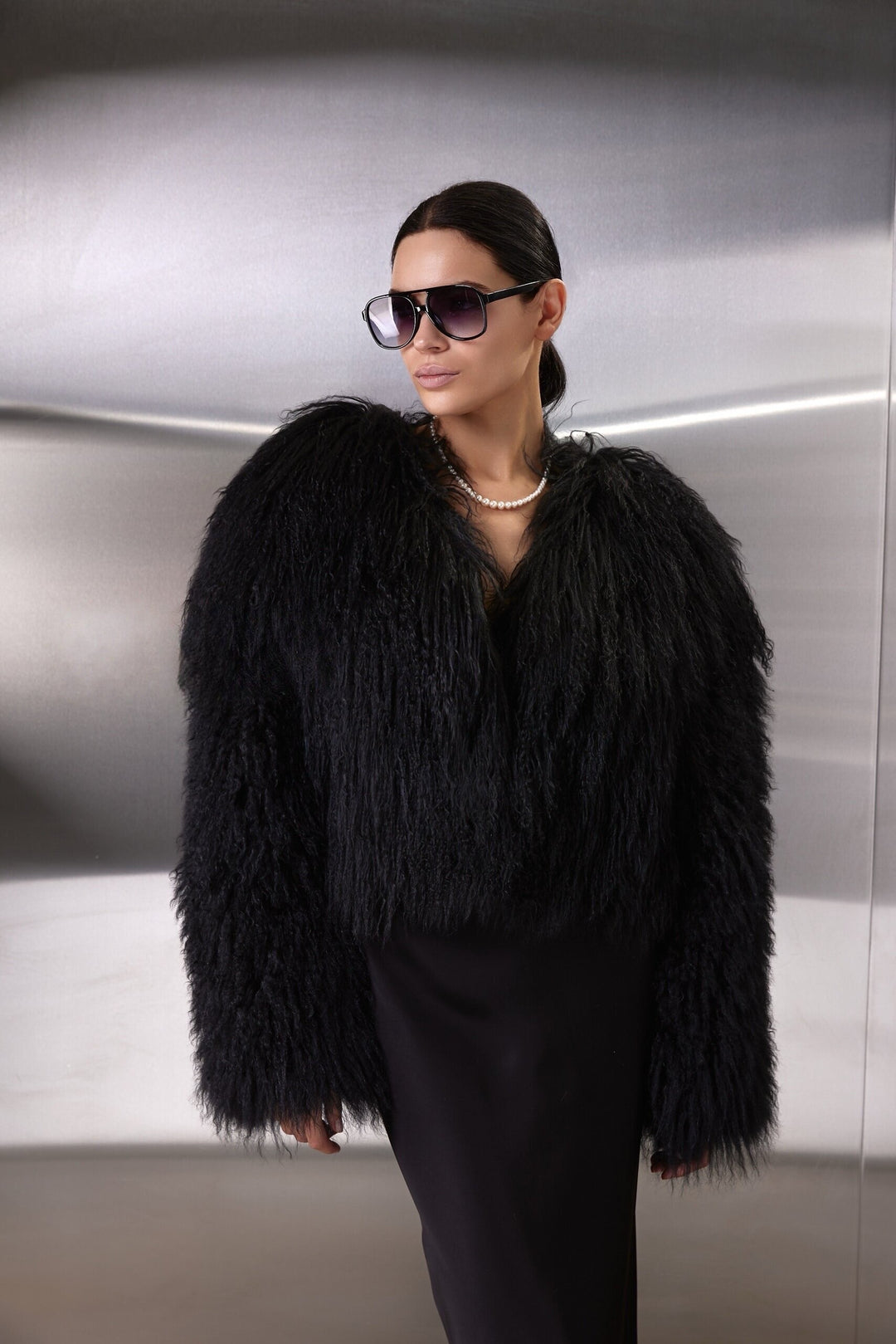 A woman wears the luxurious black Mongolian Coat, handcrafted from thick, soft 100% genuine Mongolian fur, featuring a sleek one-piece design and practical side pockets.