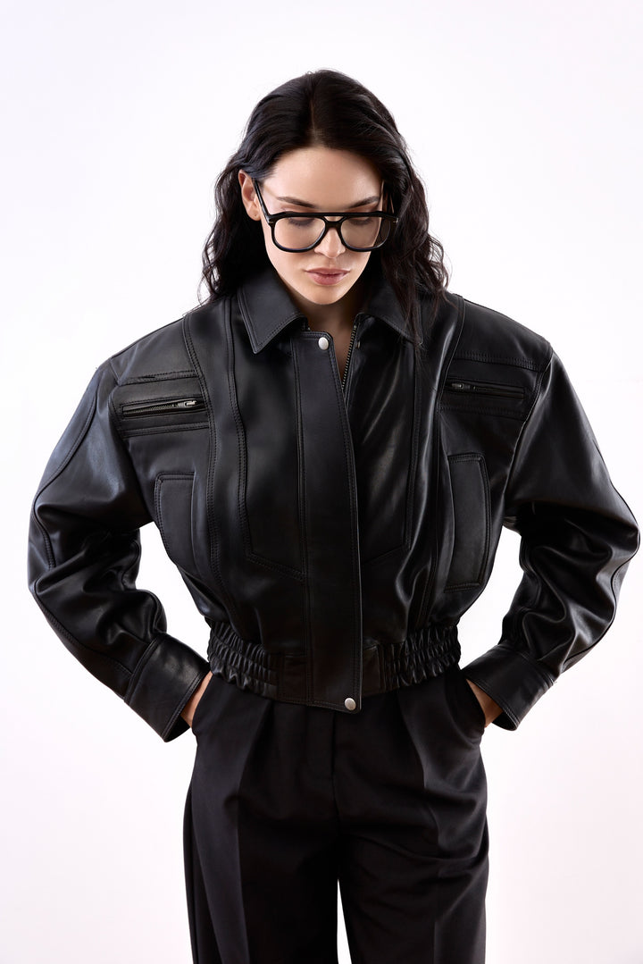 A woman wearing a cropped bomber jacket made from ultra-soft genuine leather, featuring a modern silhouette that sits just above the waist, blending contemporary edge with timeless sophistication.