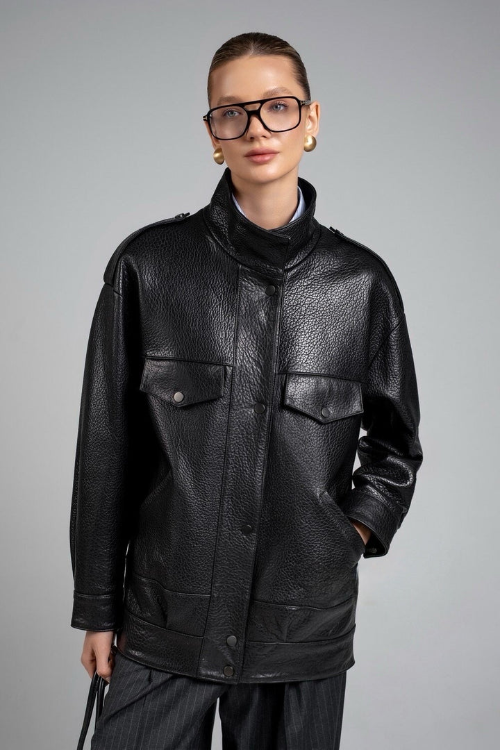 A woman wearing a sleek black genuine leather jacket with a high neck and clean lines, paired with stylish glasses for a modern, polished look.