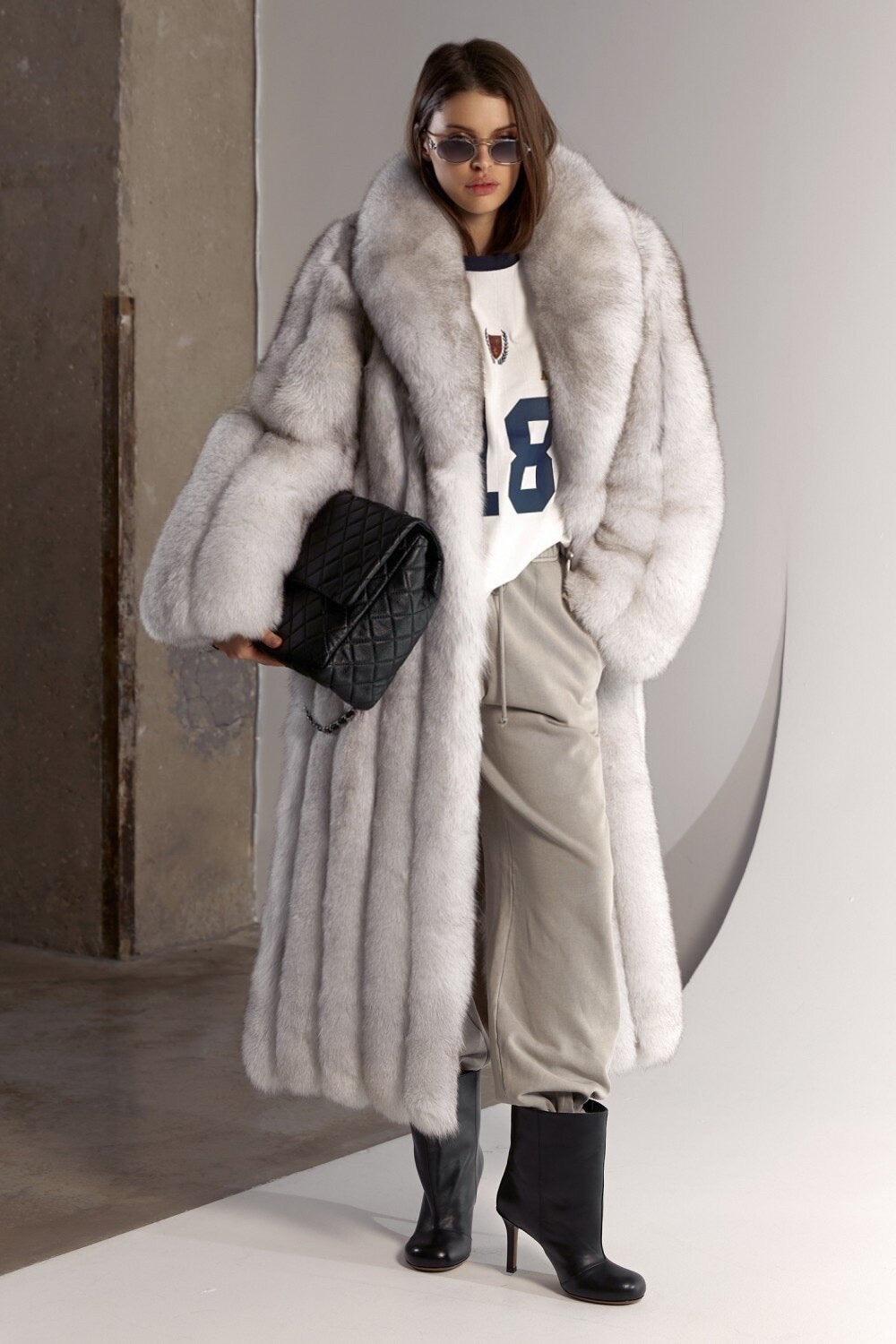 A woman wearing a luxurious natural white fox fur coat with soft mixed grey tones, featuring a sleek, elongated silhouette and plush texture for exceptional warmth.