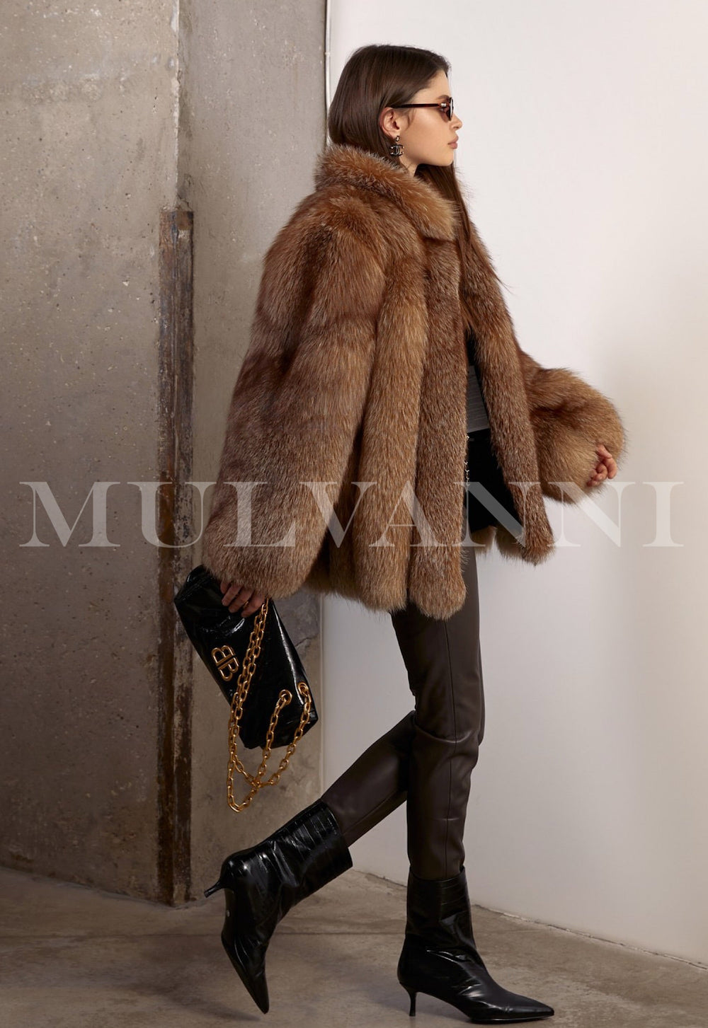 Dressed in a radiant natural fox fur coat, the woman pairs it with fitted brown leggings and a structured black leather bag for a chic, refined look.