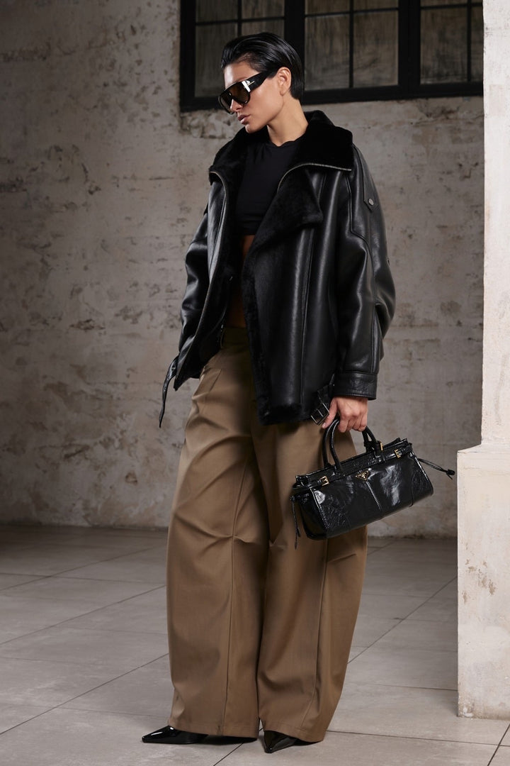 A woman wearing a relaxed-fit oversized sheepskin jacket, featuring a high neck and luxurious shearling lining, perfect for combining sporty edge with everyday elegance.