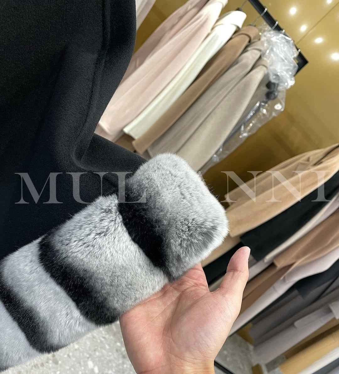 Close-up of a hand holding a black cashmere cape with rex rabbit fur trim in a clothing store featuring luxury fabrics.