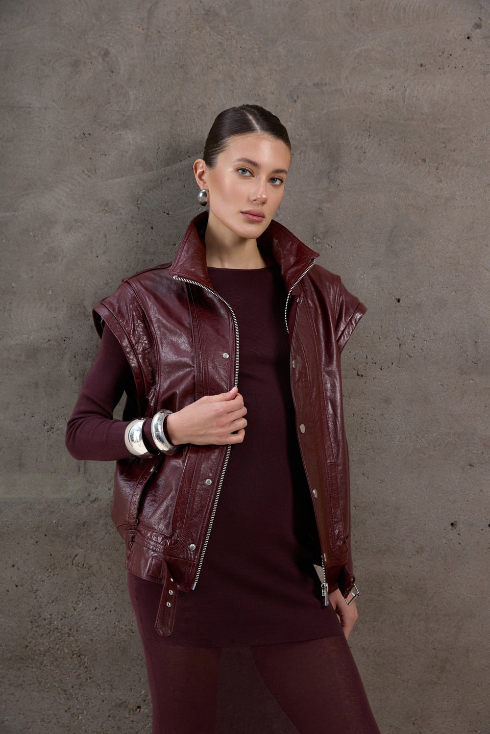 A woman wearing a versatile burgundy leather jacket with detachable sleeves, styled with a matching burgundy total look for a cohesive and chic outfit.