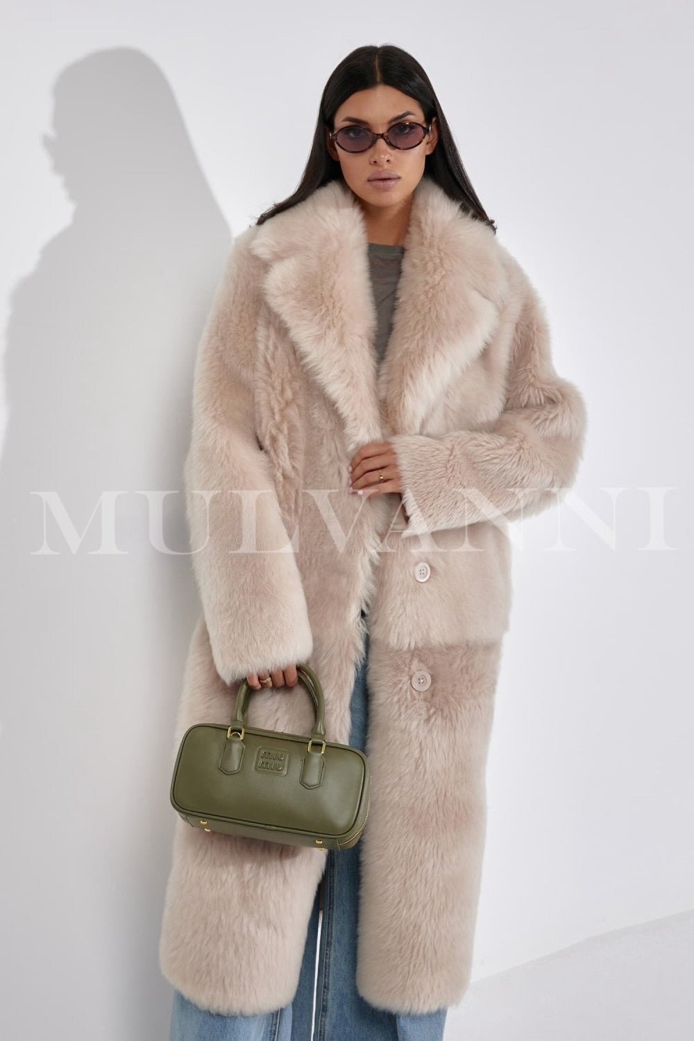 A woman wears a long, luxurious shearling coat with a thick, cozy interior and a flattering silhouette, perfect for cold weather.