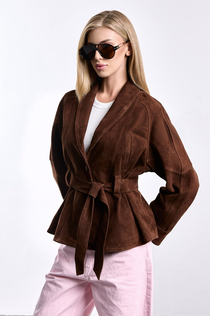 A woman models a cropped brown suede jacket, styled with a defined waist belt and clean lines, offering a refined mix of sophistication and contemporary design.