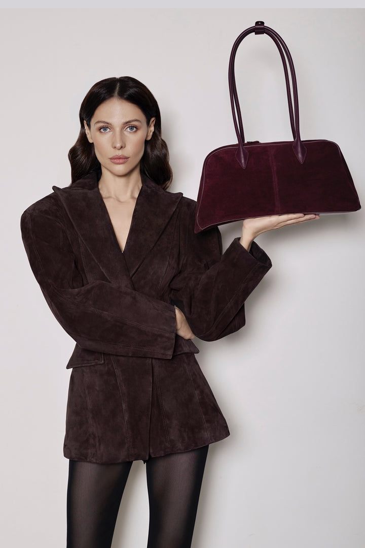 A woman dressed in a soft brown suede blazer with a cinched waist and black tights, carrying a matching brown suede bag for a coordinated and sophisticated look.