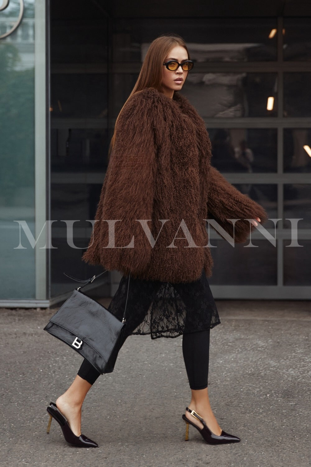 A woman wearing a high-quality brown Mongolian coat, characterized by its luxurious, fluffy texture. The coat features a tailored fit and elegant design, providing both warmth and sophistication for cold weather.