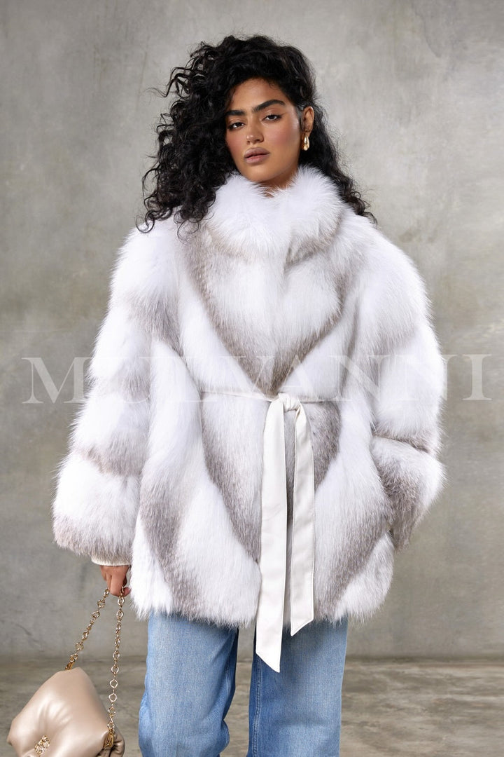 A woman wears a meticulously handcrafted crossed Arctic fox fur coat, showcasing exceptional softness and volume with a sleek, hoodless design that exudes timeless elegance and refined luxury.
