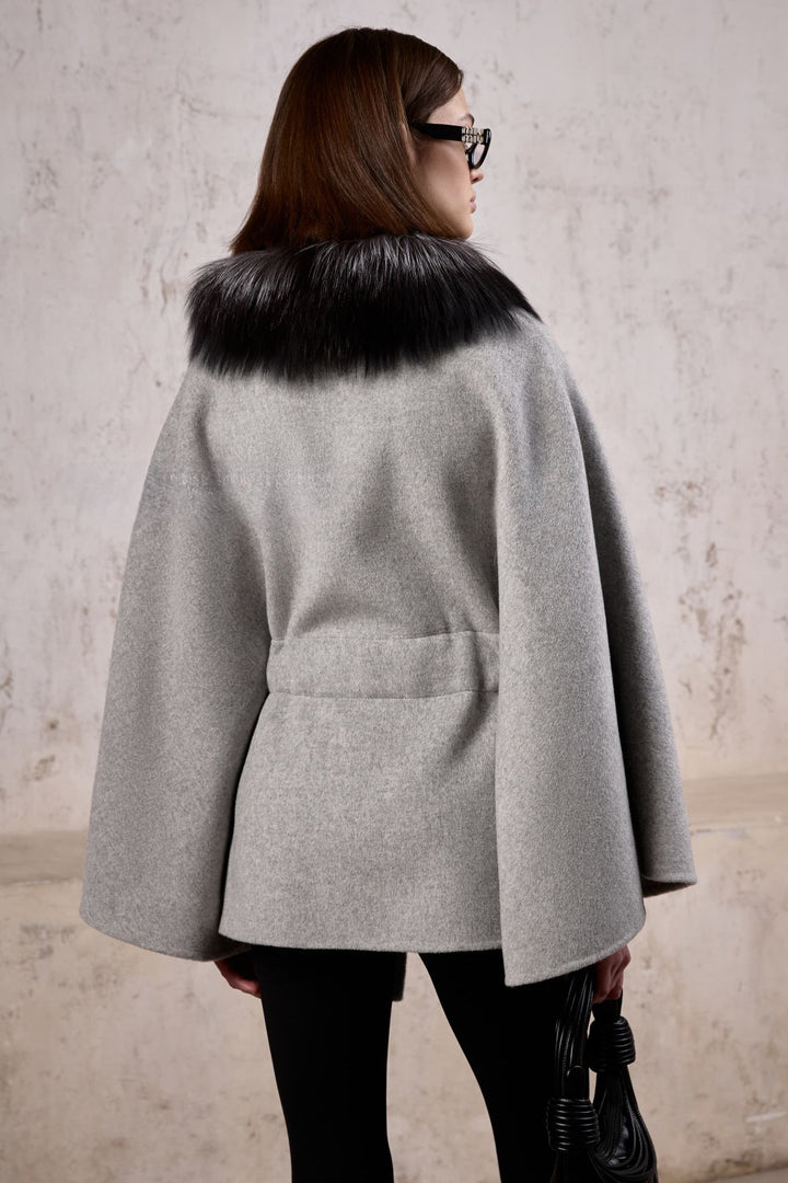 A woman is seen wearing a timeless cashmere cape featuring soft silver fox fur trim, ideal for layering over sweaters in any season.