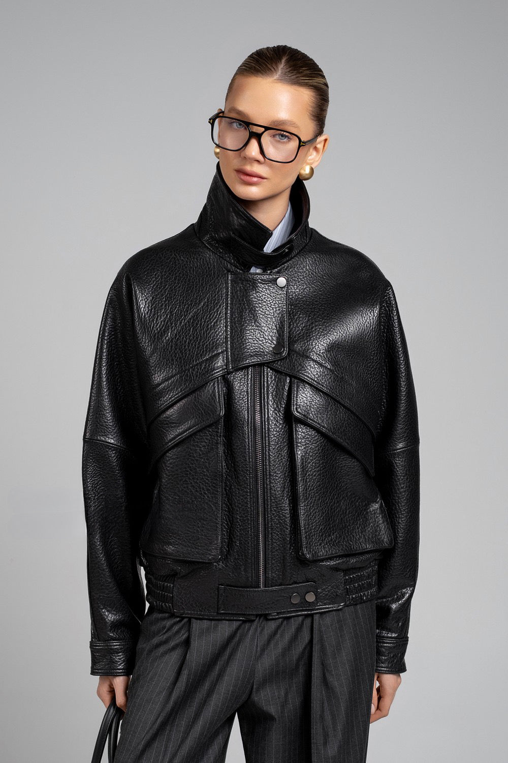 Elegant woman in cropped black leather jacket, styled with wide-leg trousers and bold sunglasses.