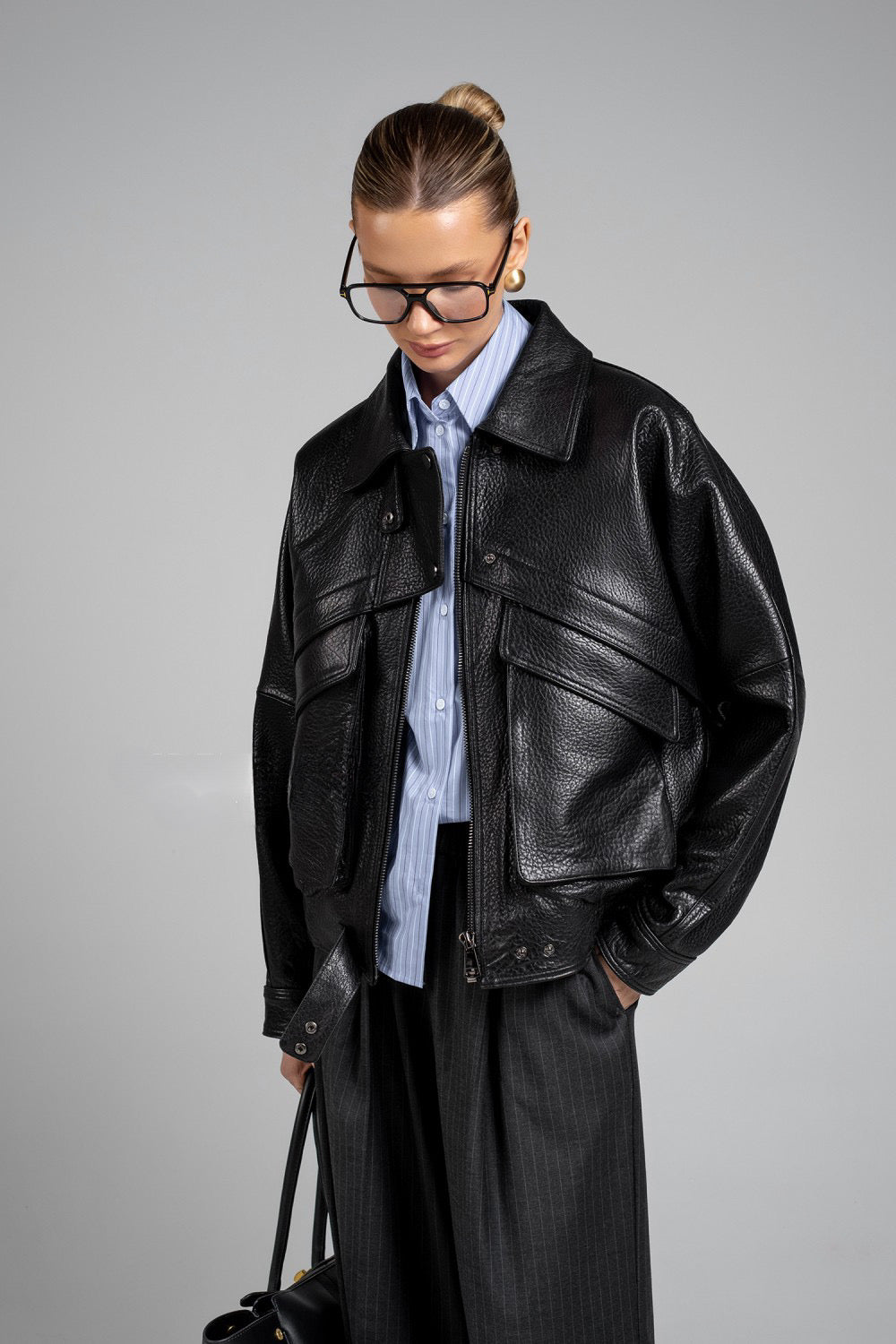 Model wearing structured black leather jacket with gold hardware, reflecting modern luxury and sleek design.