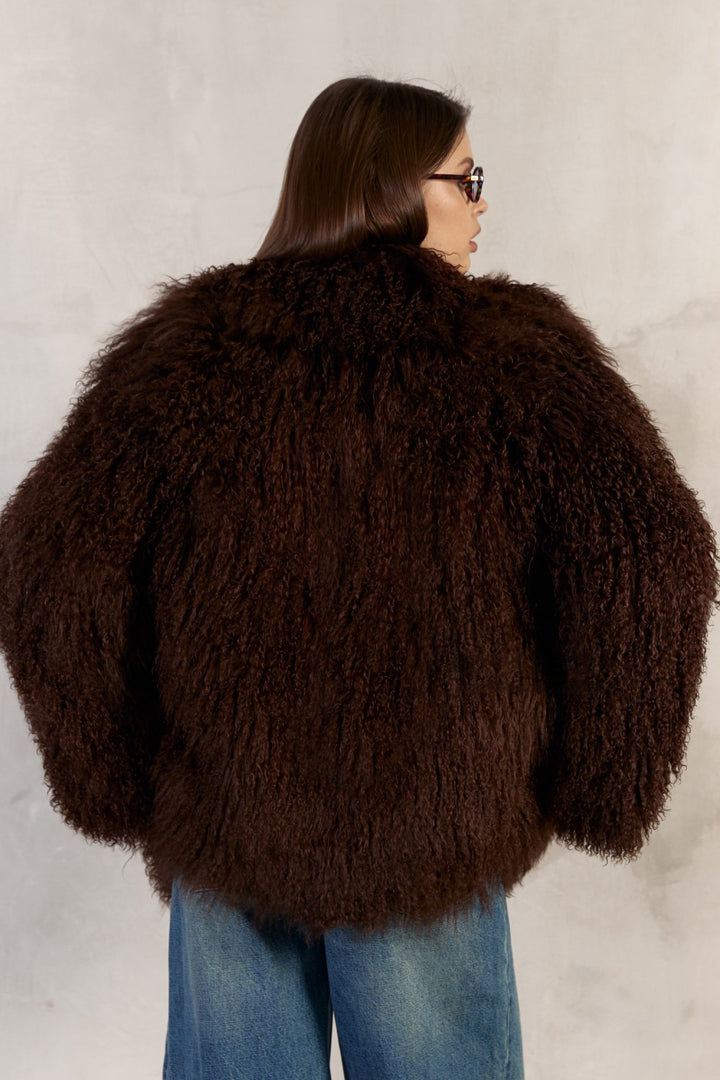 Wearing a genuine 100% Mongolian fur coat in rich brown, a woman exudes luxury with the coat’s dramatic collar, practical side pockets, and smooth satin and leather inner lining.