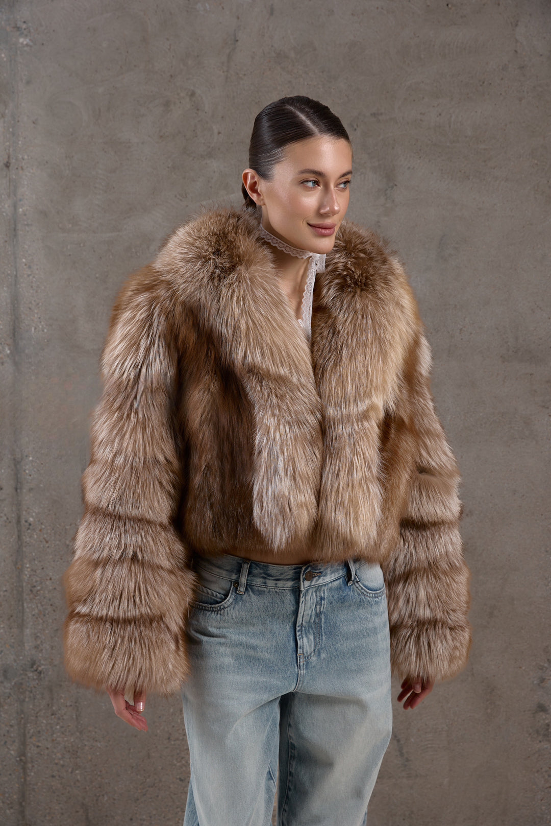 Wearing jeans and a plush short fox fur coat in natural brown shades, the woman radiates refined charm and cold-weather luxury.