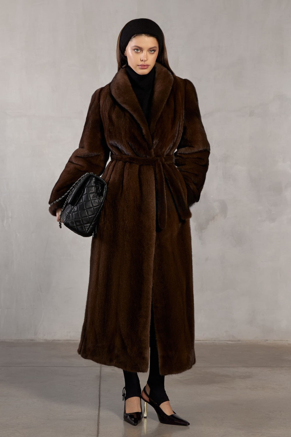 A woman wears a full-length dark brown mink fur coat, radiating elegance and warmth with its rich, velvety texture.