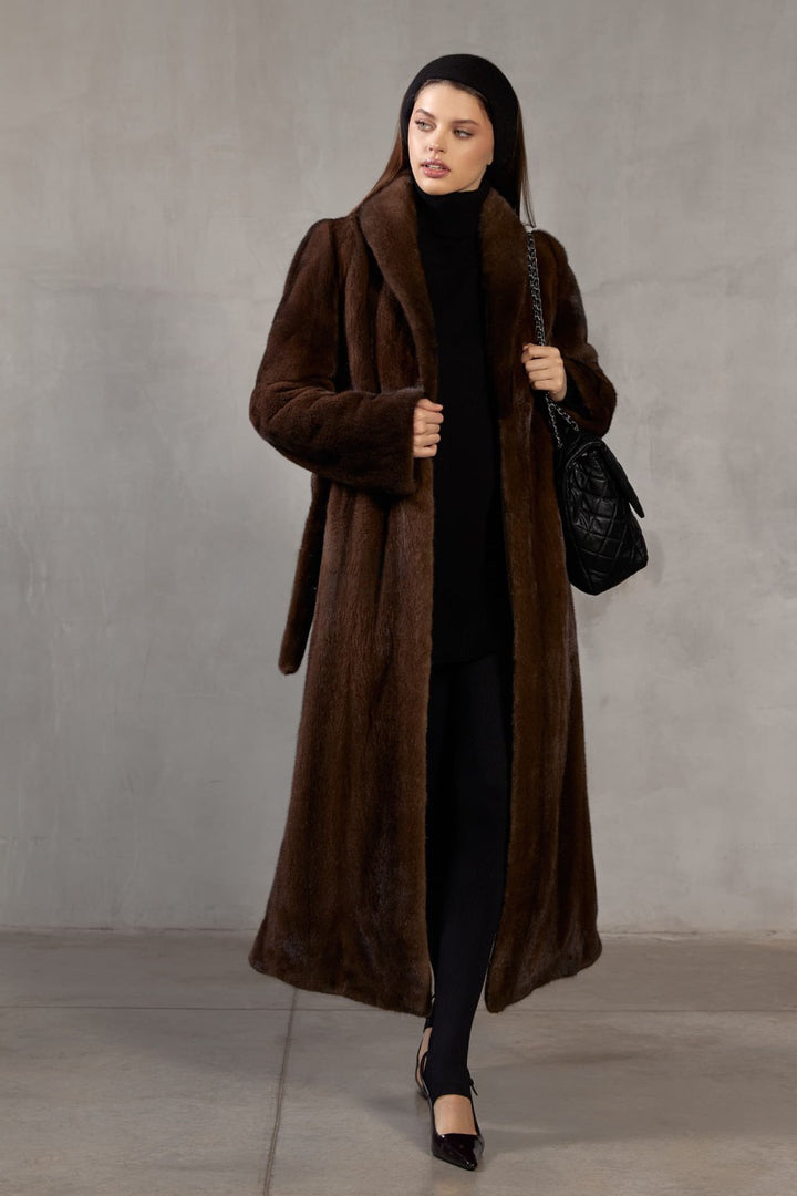 A woman stands elegantly in a floor-length dark brown mink coat, designed for both dramatic warmth and elevated style.