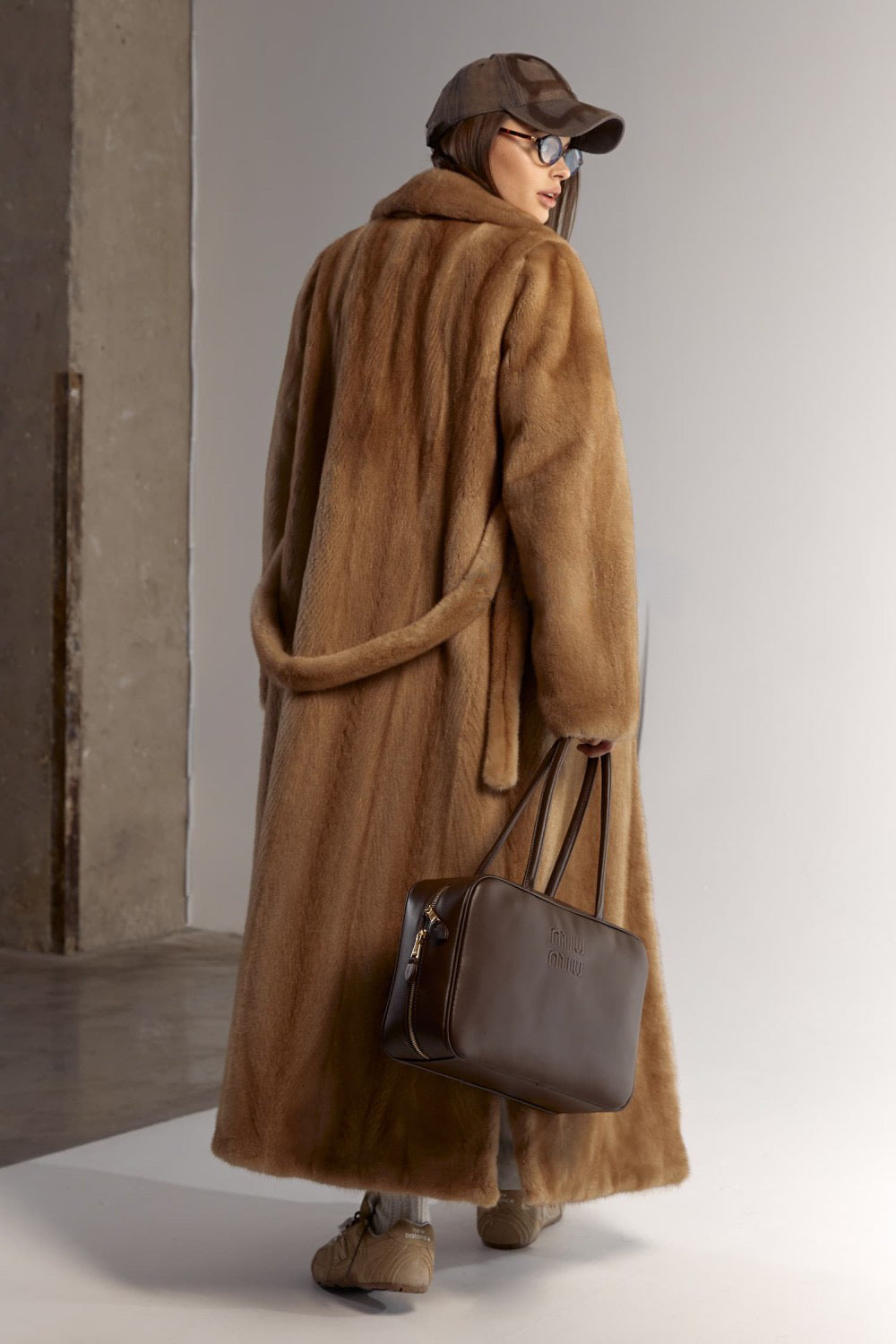 A woman elegantly wears a genuine mink fur coat with a lustrous finish and sweeping length, perfect for enduring winter in style.