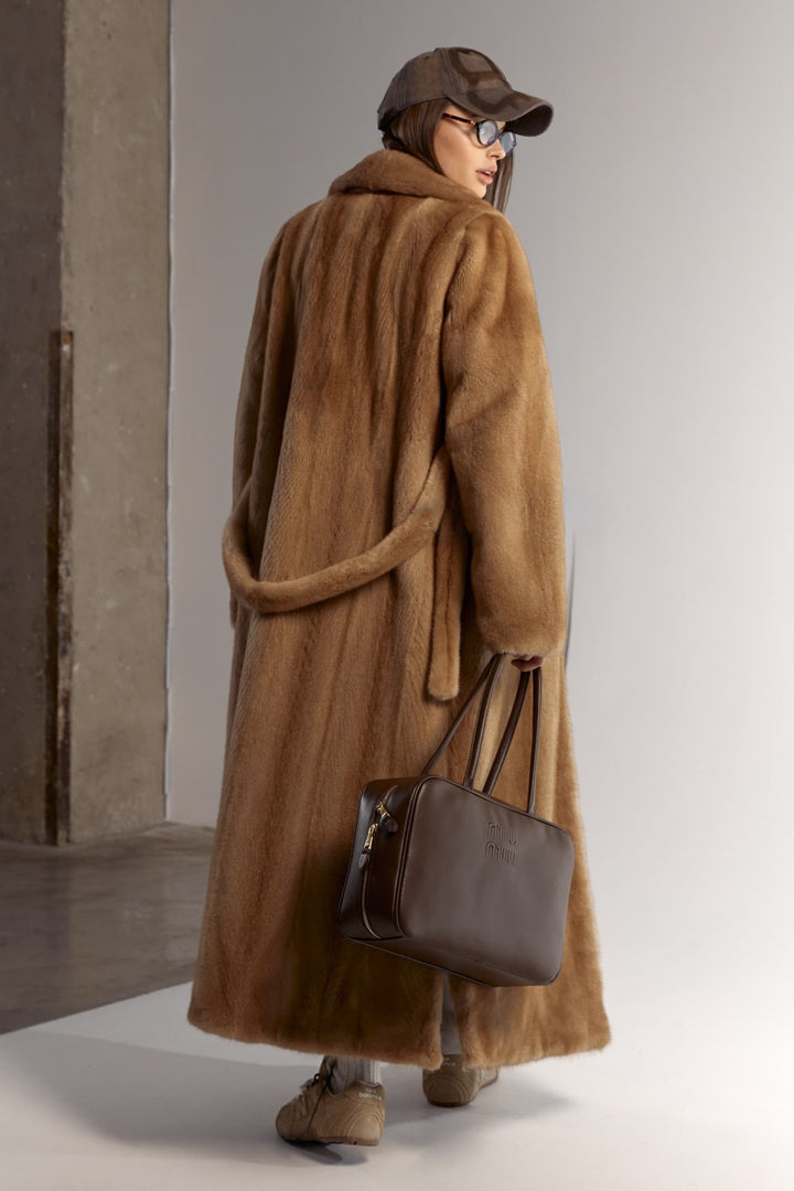 A woman elegantly wears a genuine mink fur coat with a lustrous finish and sweeping length, perfect for enduring winter in style.
