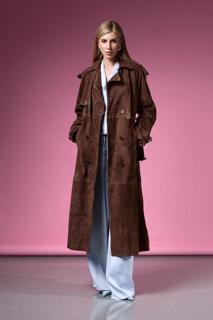 A woman dressed in a chocolate brown suede trench coat featuring high-quality leather, a structured fit, and a timeless double-breasted design.