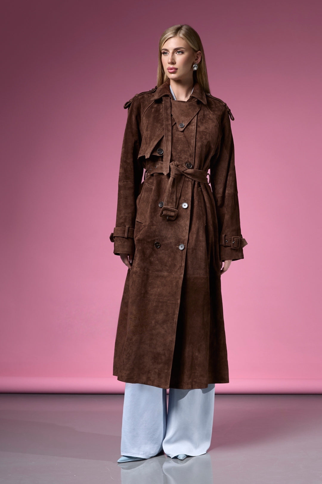 A woman wearing a chocolate brown suede leather trench coat with a double-breasted front and tailored fit, blending timeless style with modern sophistication.