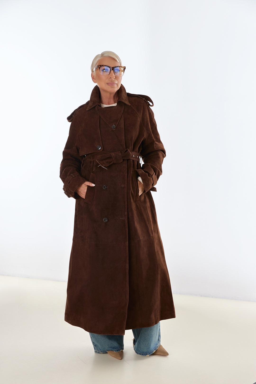 A plus size woman wearing a chocolate brown suede leather trench coat, featuring a double-breasted front and a flattering tailored fit for elegant layering.