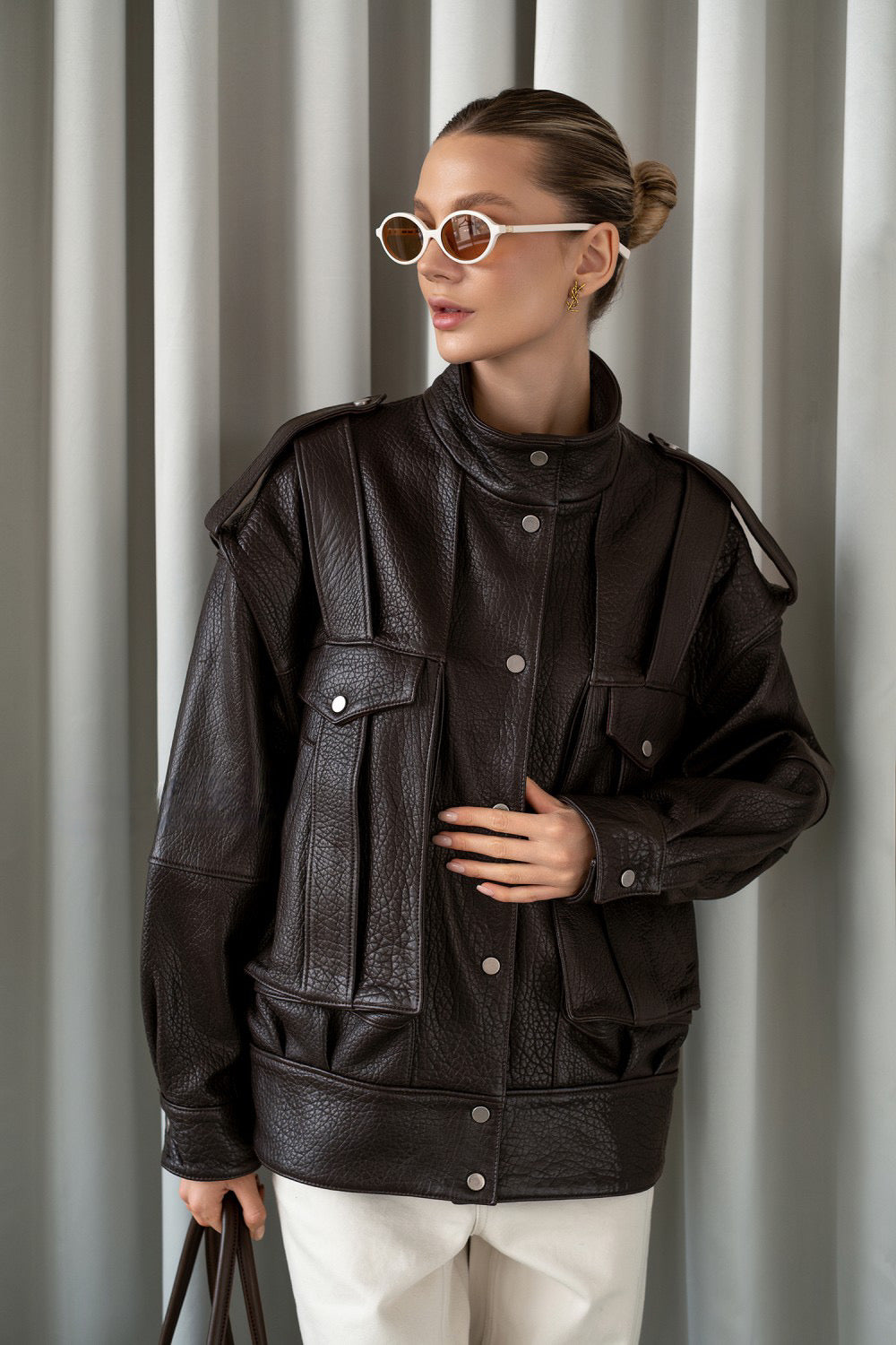 A woman wears a dark brown leather jacket styled with neutral trousers, showcasing a sleek and sophisticated everyday look.