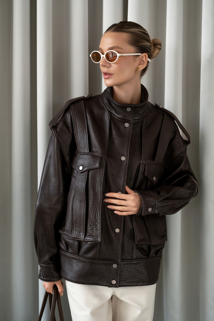 A woman wears a dark brown leather jacket styled with neutral trousers, showcasing a sleek and sophisticated everyday look.