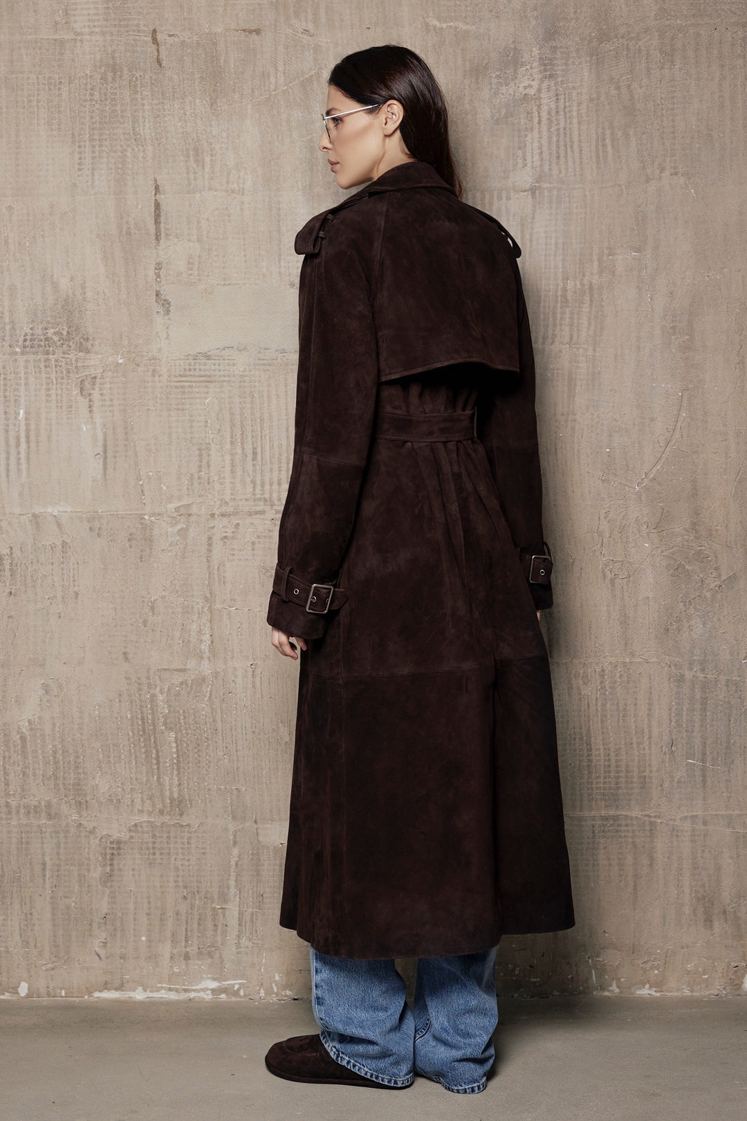 A woman models a suede leather trench coat, tailored to contour the figure while offering space for layering, crafted from high-quality suede for a timeless look.