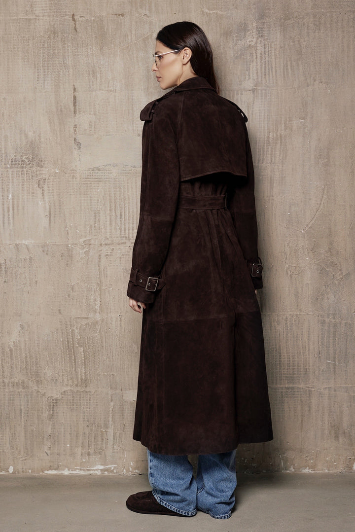 A woman models a suede leather trench coat, tailored to contour the figure while offering space for layering, crafted from high-quality suede for a timeless look.